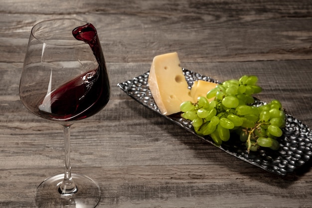 A bottle and a glass of red wine with fruits over weathered wooden surface