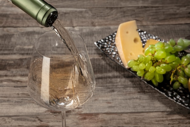 A bottle and a glass of white wine with fruits over wooden table