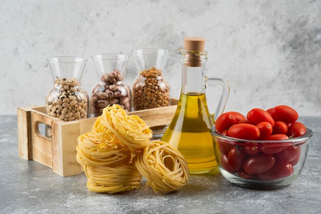 A bottle of oil with raw nest pasta and cherry tomatoes.