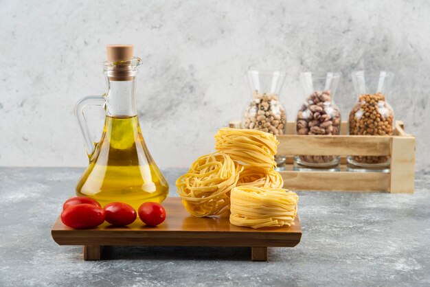 A bottle of oil with raw nest pasta and cherry tomatoes.