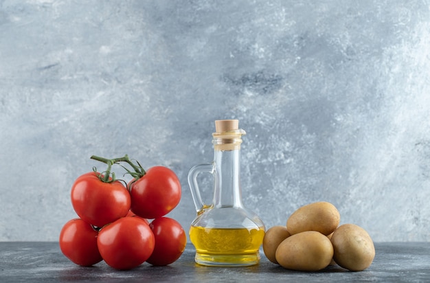 Free photo bottle of olive oil, potatoes and tomatoes on marble background