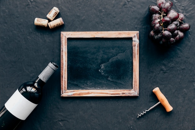 Free photo bottle with grape and corkscrew around blackboard