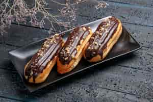 Free photo bottom close view chocolate eclairs on rectangle plate on the dark wooden table