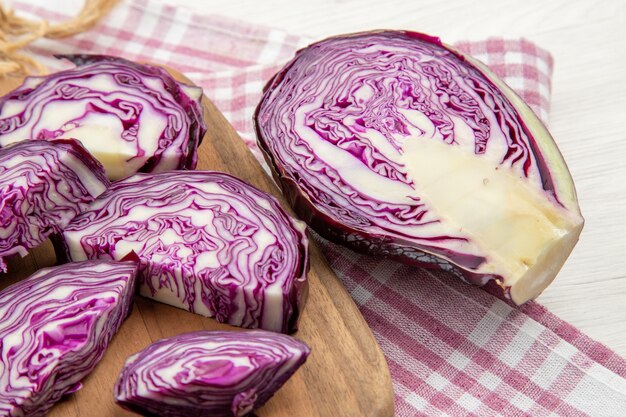 Bottom close view chopped red cabbage knife on wooden board on pink white checkered kitchen towel on grey table