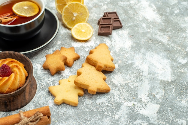 Bottom close view a cup of tea lemon slices cinnamon sticks cookies chocolate on grey surface free space