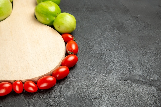 Bottom close view green and red tomatoes around a chopping board on dark background