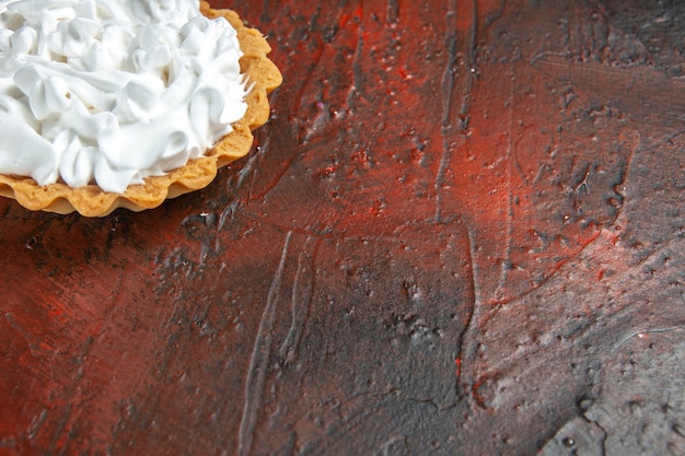 Bottom close view small tart with pastry cream on dark red table copy space