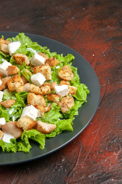 Bottom half view caesar salad on oval plate on dark red table