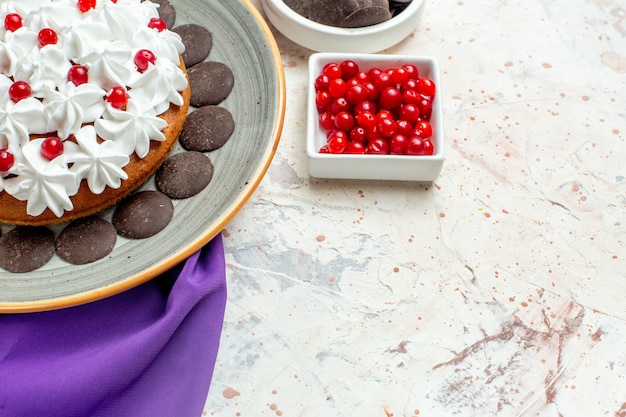 Bottom half view cake with pastry cream on oval plate purple shawl chocolate and berries in bowls on white table