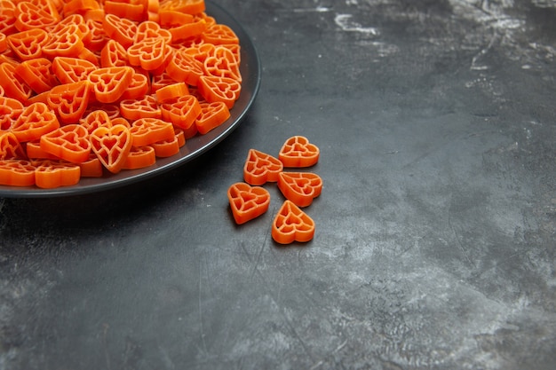 Bottom half view heart shaped red italian pasta on black oval plate on dark surface