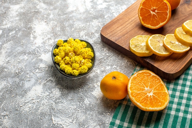 Free Photo bottom half view oranges lemon slices on wood board yellow candies in bowl on grey surface