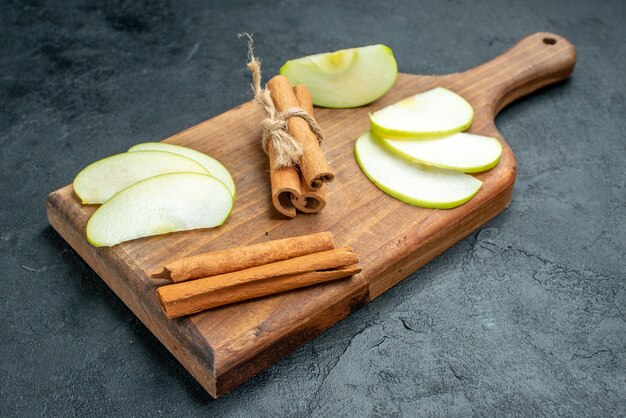 Bottom view apple slices and cinnamon sticks on chopping board on dark table