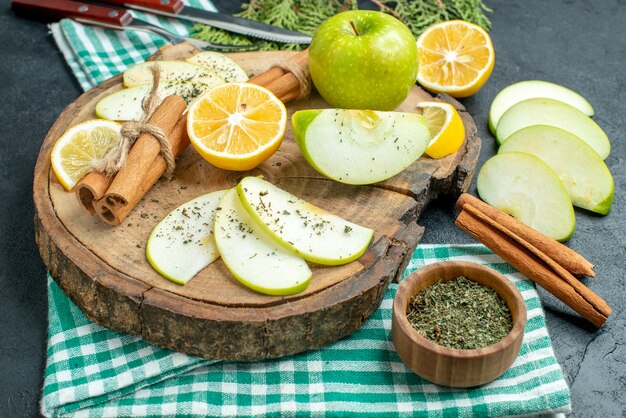 Bottom view apple slices cinnamon sticks and lemon slices apple on wood board a fork and knife on green napkin on black ground