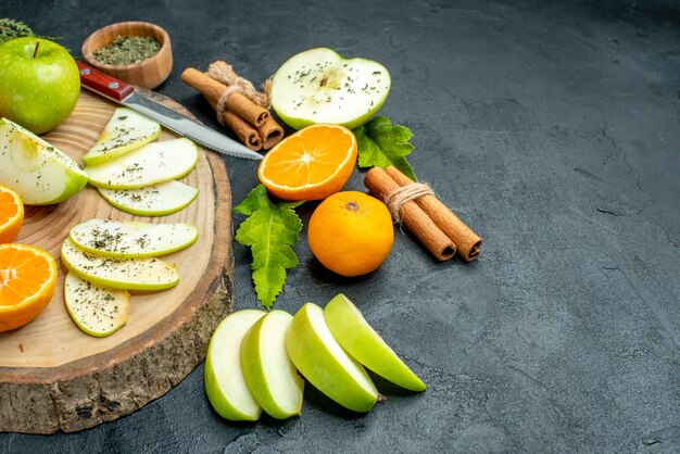 Bottom view apple and tangerine slices knife on wood board cinnamon sticks tied with rope dried mint powder on black table free space