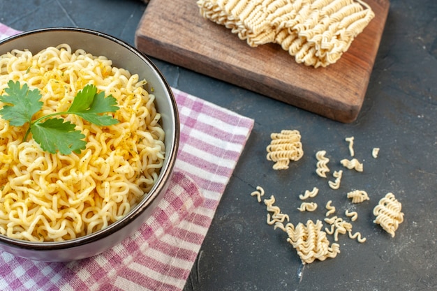 Bottom view asian ramen noodles in bowl on pink white checkered tablecloth raw ramen noodle on cutting board on dark table