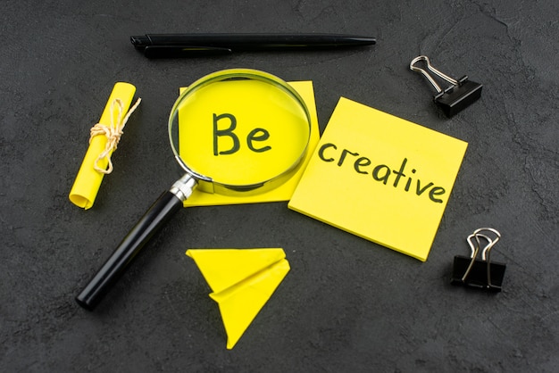 Free photo bottom view be creative written on yellow sticky note lupa binder clips pen on dark background