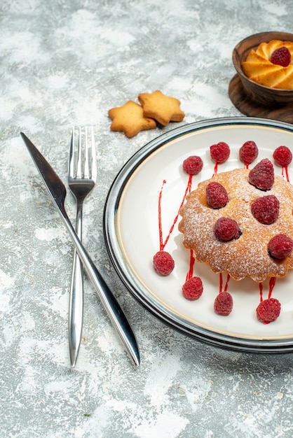 Free Photo bottom view berry cake on oval plate raspberries in bowl crossed fork and dinner knife on grey surface