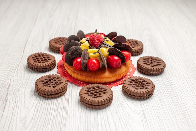 Bottom view berry cake on the red oval lace doily and cookies on the white wooden table