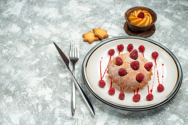 Bottom view berry cake on white oval plate biscuits crossed fork and dinner knife on grey surface free space