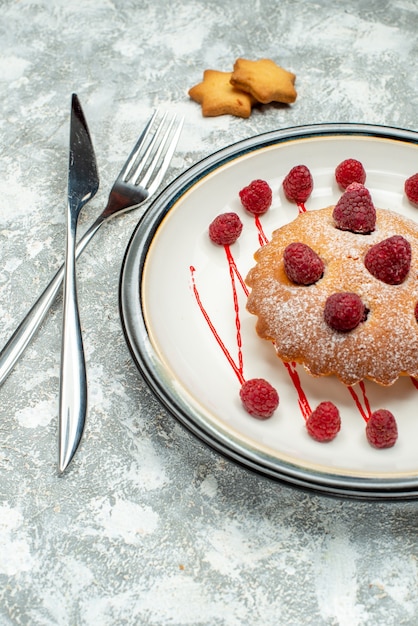 Bottom view berry cake on white oval plate crossed fork and dinner knife on grey surface