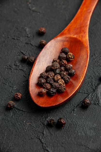 Free Photo bottom view black pepper on wooden spoon on black surface