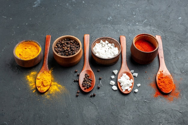 Free Photo bottom view bowls with turmeric black pepper sae salt red pepper powder wooden spoons on black surface