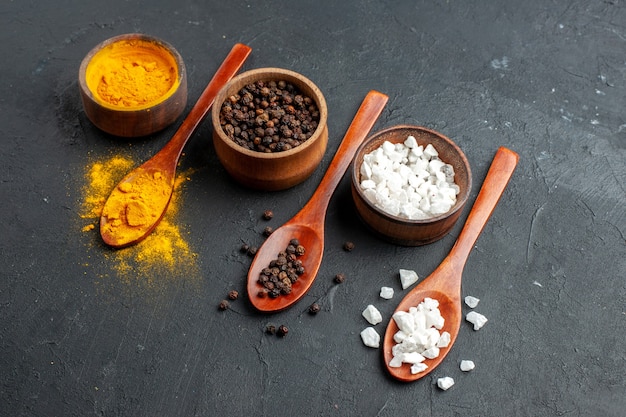 Free Photo bottom view bowls with turmeric black pepper sae salt wooden spoons on dark surface