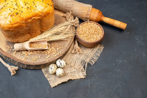 Bottom view bread with black cumin on natural wood board wheat grains in bowl rolling pin quail eggs on table with copy place