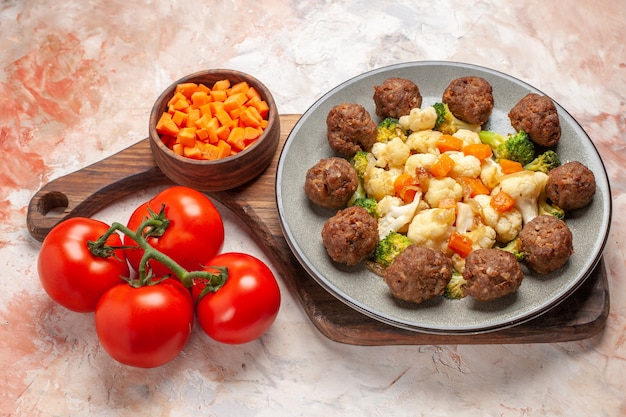 Free Photo bottom view broccoli and cauliflower salad and meatball on plate cutting carrot in bowl on cutting board tomatoes on nude background