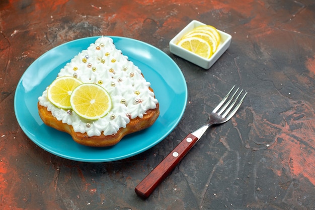 Bottom view cake with lemon on blue plate lemon slices in bowl fork on dark red background