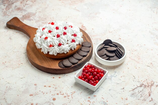 Bottom view cake with pastry cream and chocolate on chopping board bowls with berries and chocolate on light grey surface