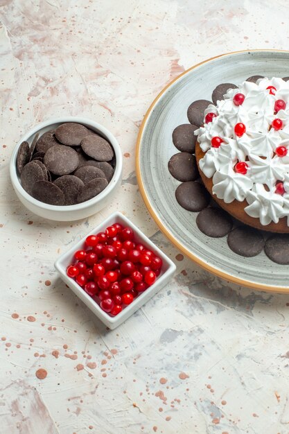 Bottom view cake with pastry cream on oval plate berries and chocolate in bowls on beige table