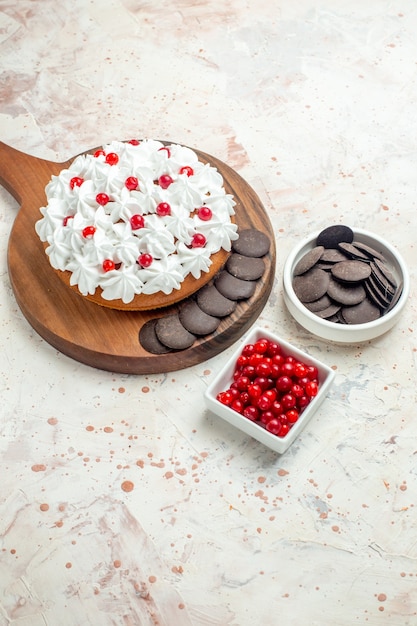 Bottom view cake with white pastry cream and chocolate on chopping board bowls with berries and chocolate on light grey surface