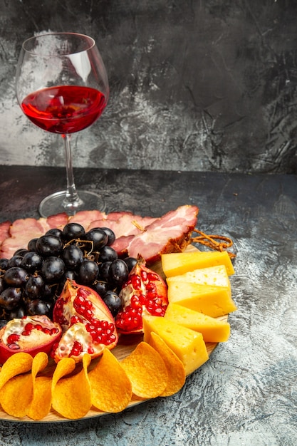 Free Photo bottom view cheese pieces meat grapes and pomegranate on oval serving board glass of wine on dark background