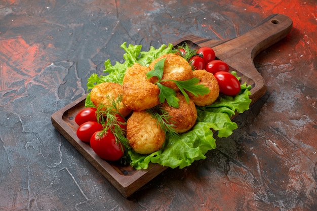 Bottom view chicken nuggets lettuce cherry tomatoes on cutting board on dark table with copy space