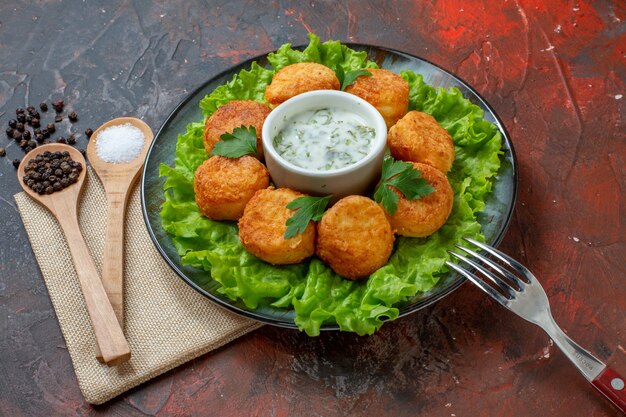 Bottom view chicken nuggets lettuce fork on plate salt and black pepper in wooden spoons on dark table