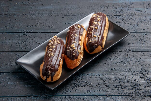 Bottom view chocolate eclairs on rectangle plate on the dark wooden table with free space