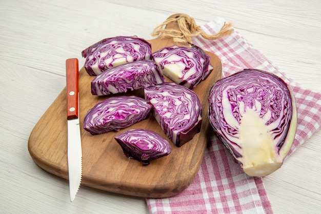 Bottom view chopped red cabbage knife on wooden board on pink white checkered kitchen towel on grey table