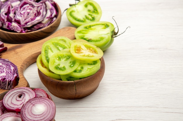 Free photo bottom view chopped red cabbages cut onion cut green tomatoes in bowls on white surface