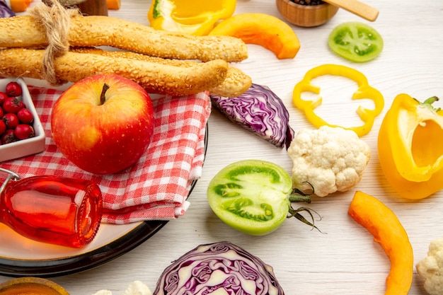 Bottom view chopped vegetables apple bread red bottle on napkin on round plate on white table