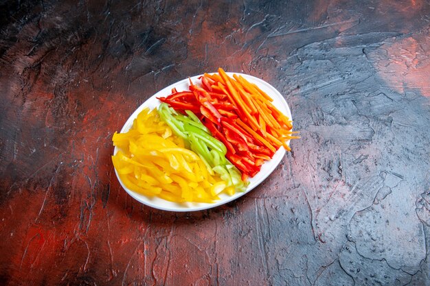 Bottom view colorful cut peppers on white plate on dark red table free place