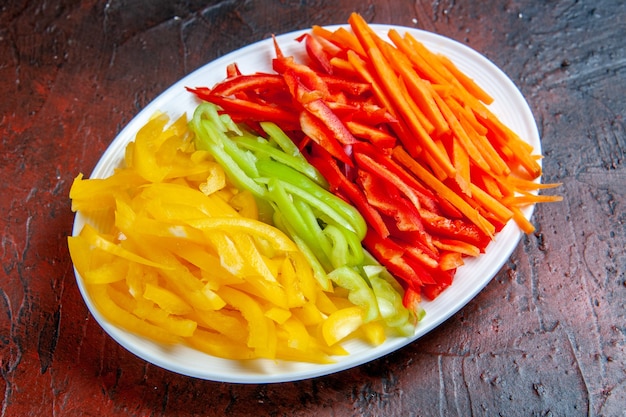 Bottom view colorful cut peppers on white plate on dark red table