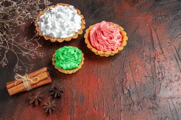 Bottom view colorful tarts star anises cinnamon sticks on dark red table with free space