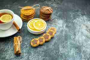 Free photo bottom view cup of tea flavored by lemon biscuits with chocolate cookies tied with rope cinnamon sticks lemon slices on grey table free place