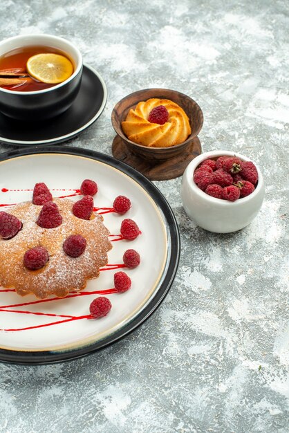 Bottom view a cup of tea with lemon slices and cinnamon sticks berry cake on oval plate on grey surface