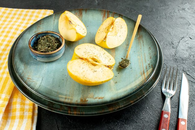 Bottom view cut apples dried mint in bowl wooden spoon on plate knife and a fork yellow kitchen towel on dark ground