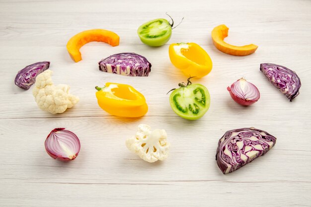 Bottom view cut vegetables red cabbage cauliflower yellow bell pepper green tomato red onion on white wooden surface