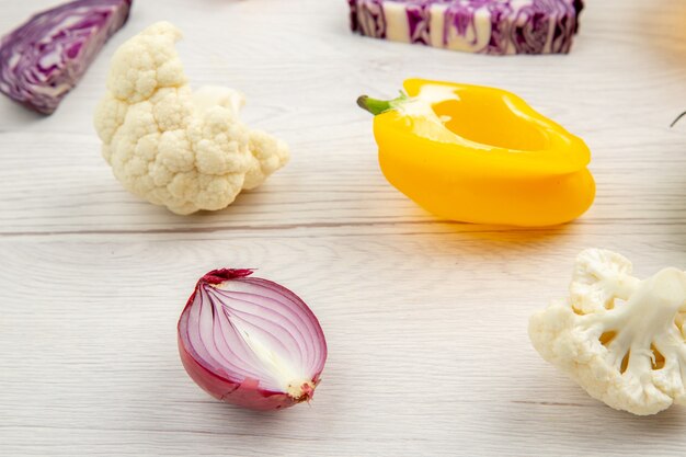 Bottom view cut vegetables red cabbage cauliflower yellow bell pepper red onion on white wooden surface