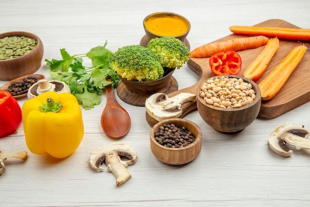 Bottom view cut yellow carrots on chopping board mushrooms black pepper in wooden spoon bowls with spices and beans broccoli on grey table