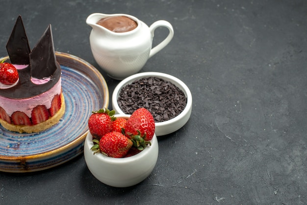 Bottom view delicious cheesecake with strawberry and chocolate on plate bowls with chocolate strawberries dark chocolate on dark isolated background free place